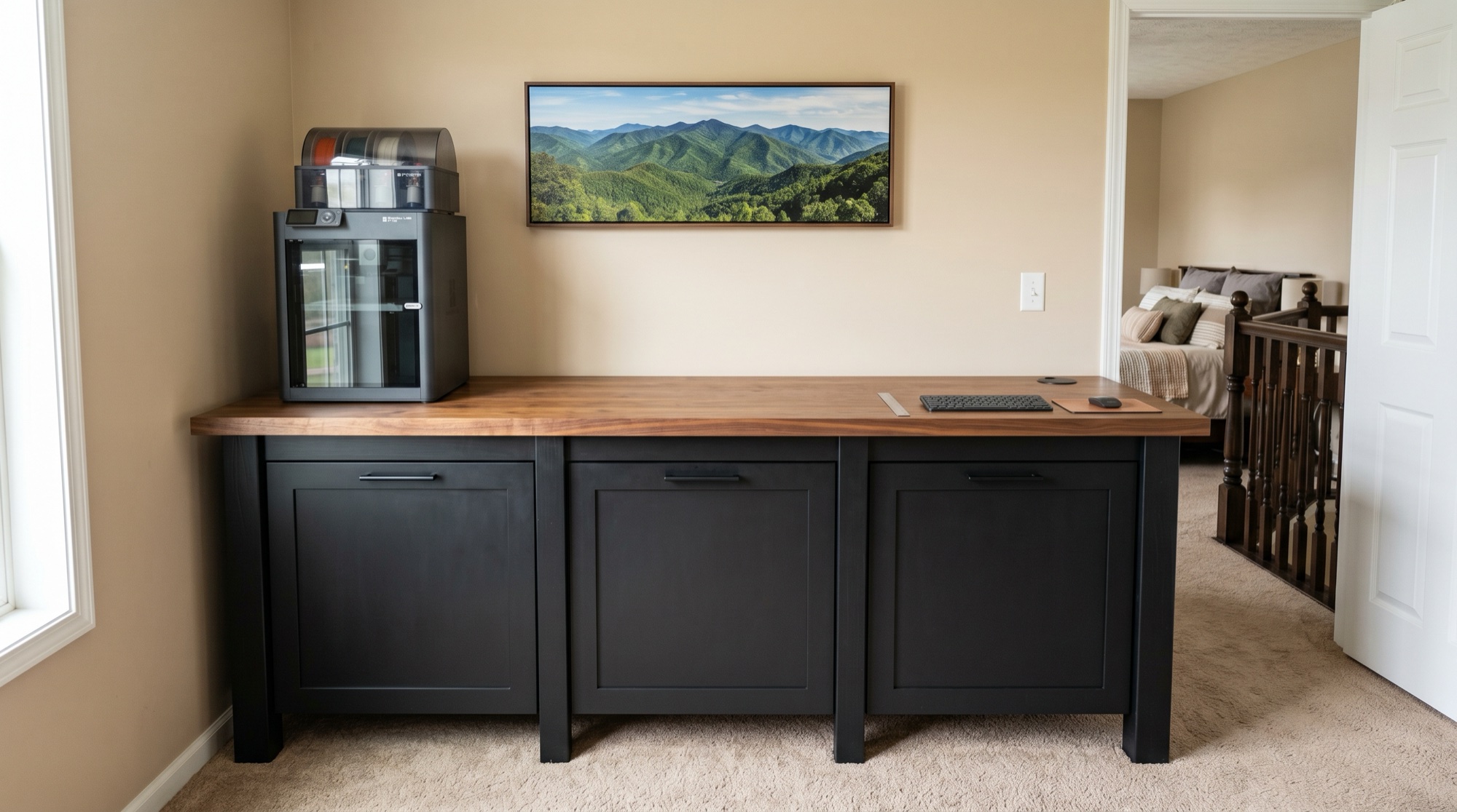 Finished standing-height workbench in a residential bedroom: matte-black frame with walnut top, three closed cabinet doors, Bambu Lab 3D printer on the counter, mountain canvas on the wall above.